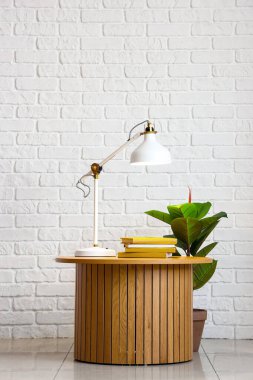 Parlayan lamba, kitaplar ve beyaz tuğla duvarın yanındaki çiçekli masa.