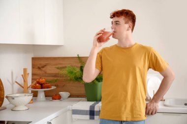 Genç kızıl saçlı adam mutfakta meyve suyu içiyor.