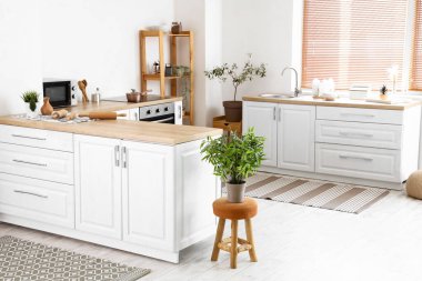 Beyaz tezgahları ve halıları olan aydınlık mutfağın içi.