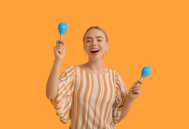 Turuncu arka planda marakas olan güzel bir genç kadın.