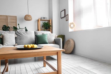 Oturma odasının iç tarafındaki ahşap sehpada limonlu rahat gri kanepe ve tabak.