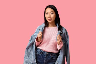 Pembe arka planda şık kot elbiseli güzel, mutlu Asyalı kadın.