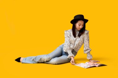 Şık kotlu, dergisi sarı arka planda oturan güzel Asyalı kadın.