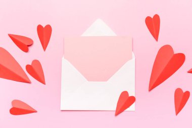 İçinde boş kart ve pembe arka planda kırmızı kağıt kalpler olan bir zarf. Sevgililer Günü kutlaması
