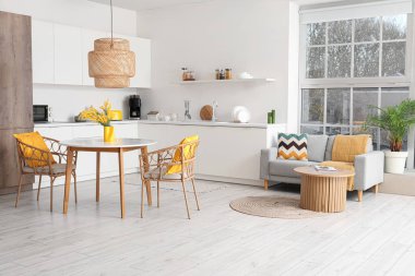 Masası, koltukları, mimoza çiçekleri, ev bitkisi, tezgahları ve kanepesi olan geniş, şık bir mutfak stüdyosu.