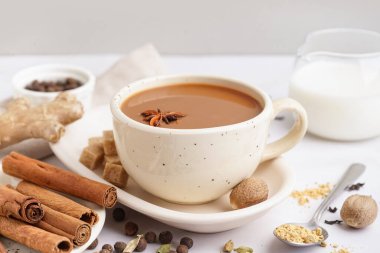 Arka planda farklı baharatlar olan bir fincan lezzetli masala çayı, yakın plan.