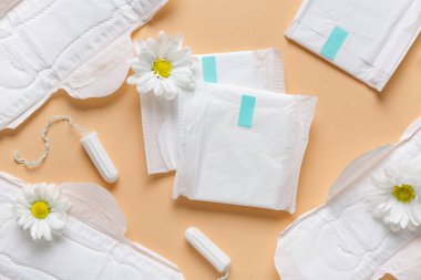 Tamponlu regl pedleri ve bej arka planda kasımpatı çiçekleri.