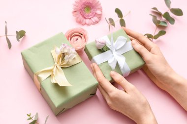 Hediye kutuları ve pembe arka planda güzel çiçekler olan kadın elleri. Uluslararası Kadınlar Günü