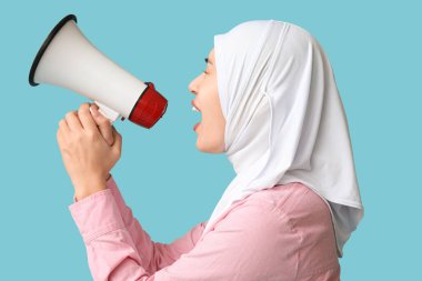 Genç Asyalı Müslüman kadın mavi arka planda megafona bağırıyor. Ulusal Duyulma Günü