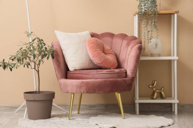 Yastıklı koltuk, dekorasyonlu raf ünitesi ve oturma odasındaki bej duvarın yanına bitki.