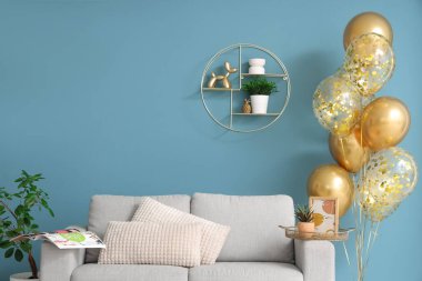 Modern oturma odasındaki mavi duvarın yanında altın renkli balonlar ve rahat kanepe.