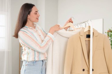 Genç bir kadın yatak odasında elbise topluyor.