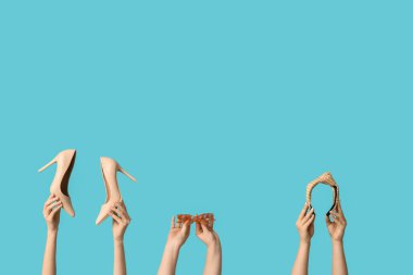 Güneş gözlüklü, bantlı ve mavi arka planda topuklu ayakkabılı kadın elleri.