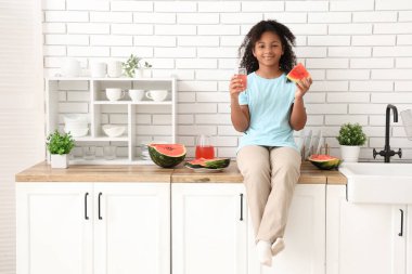 Tatlı bir karpuz parçası ve mutfakta bir bardak meyve suyu olan tatlı Afro-Amerikalı kız.