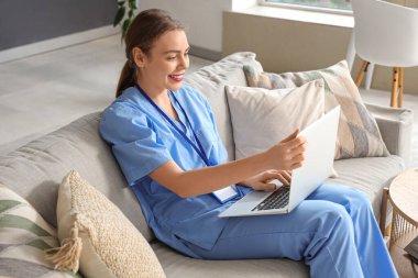 Genç bayan tıp öğrencisi evdeki koltukta modern dizüstü bilgisayar kullanıyor.