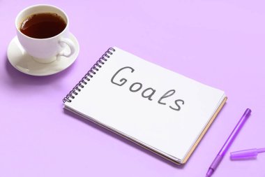 Metin hedefli defter, bir fincan çay ve leylak arkaplanlı kalem