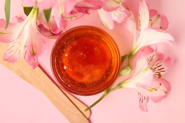 Cam kâse şekerleme macunu, tahta çubuklar ve pembe arka planda çiçekler, yakın plan.