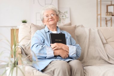 Evdeki kanepede oturan İncil 'li son sınıf öğrencisi kadın.