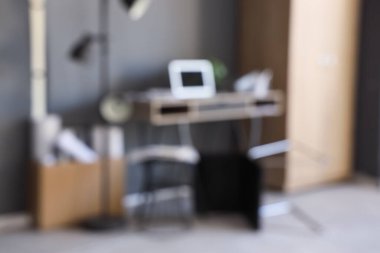 Ofiste siyah duvarın yanında dizüstü bilgisayarı ve sandalyesi olan dağınık iş yeri, bulanık görünüm