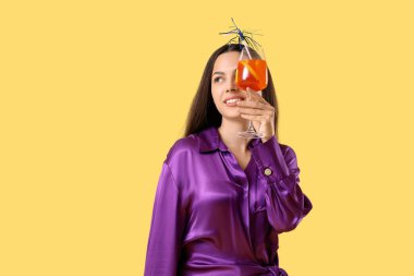 Sarı arka planda aperol sprey kokteyli olan genç bir kadın.