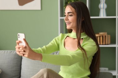 Diastemalı genç bir kadın evdeki kanepede selfie çekiyor.