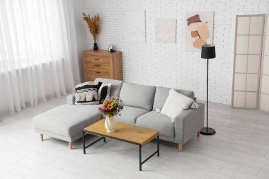 Oturma odasındaki sehpada yabani çiçekler olan rahat bir kanepe ve vazo.