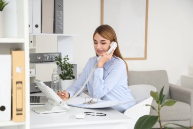 Dosyası olan genç bir iş kadını ofiste telefonla konuşuyor.