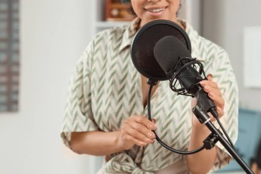 Kayıt stüdyosunda mikrofonlu genç bir kadın şarkı söylüyor.