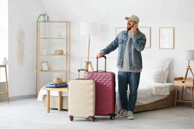 Otel odasında bavullu bir erkek turist cep telefonuyla konuşuyor.