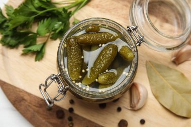 Lezzetli salatalıklı kavanoz ve beyaz ahşap arka planda farklı baharatlar.