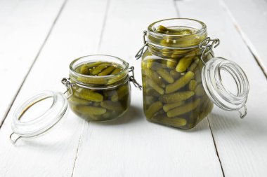 Beyaz ahşap arka planda lezzetli salatalıklı kavanozlar.