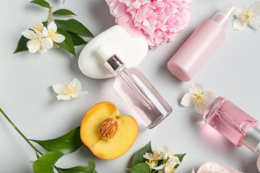 Çiçekli doğal kozmetik ürünleri, gri arka planda şeftali ve spa taşları