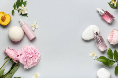 Çiçekli doğal kozmetik ürünleri, gri arka planda şeftali ve spa taşları ve metin için boşluk.
