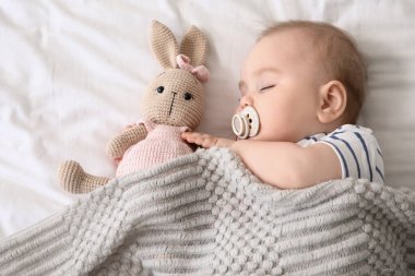 Oyuncak tavşanı ve battaniyesi olan şirin bir bebek. Yatakta uyuyor.