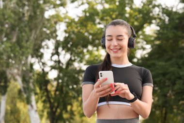 Dışarıda cep telefonu kullanan kulaklıklı bir kadın koşucu.