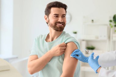 Genç adam klinikteki doktordan aşı alıyor.
