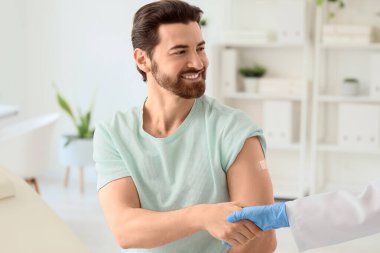 Uygulamalı tıbbi yaması olan genç bir adam ve klinikteki aşıdan sonra tokalaşan bir doktor.