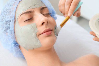 Güzellik uzmanı kuaförde kadının yüzüne maske takıyor.