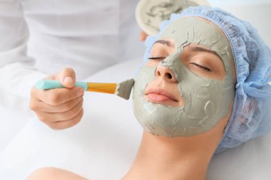 Güzellik uzmanı kuaförde kadının yüzüne maske takıyor.