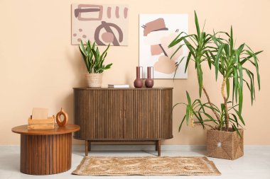 Oturma odasının içinde ev bitkileri, tuvalet, ahşap masa ve bej duvarın yanında hasır halı var.