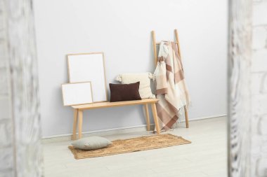 Beyaz duvarın yanında ahşap bank, merdiven, çerçeve ve hasır halı olan oturma odasının içinde.