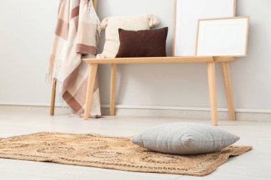 Beyaz duvarın yanında ahşap bank, merdiven, çerçeve ve hasır halı olan oturma odasının içinde.