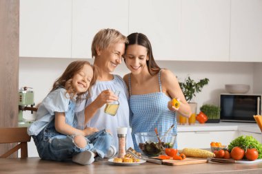 Annesi ve büyükannesiyle birlikte mutfakta sebze salatası yapan küçük bir kız.