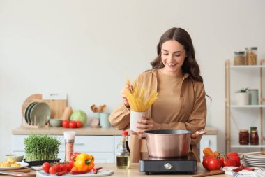 Genç bir kadın mutfakta spagetti pişiriyor.