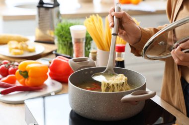 Genç kadın mutfakta erişte çorbası yapıyor, yakın plan.