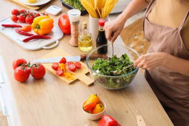 Genç bir kadın mutfakta sebze salatası yapıyor.