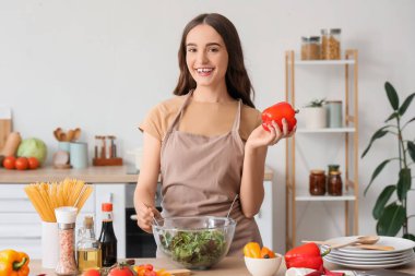 Biberli genç bir kadın mutfakta sebze salatası yapıyor.