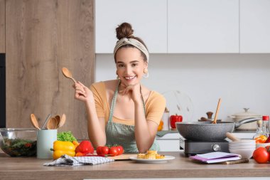 Mutfaktaki masada kaşığı ve sebzesi olan genç bir kadın.