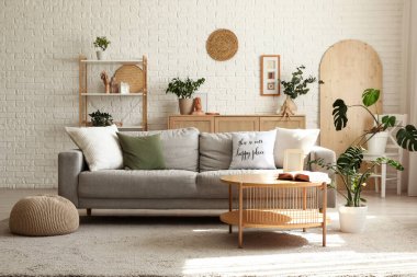 Gri kanepe, ahşap masa ve bitkilerle aydınlık oturma odasının içinde.