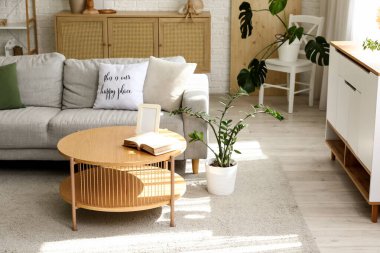 Gri kanepe, ahşap masa ve bitkilerle aydınlık oturma odasının içinde.